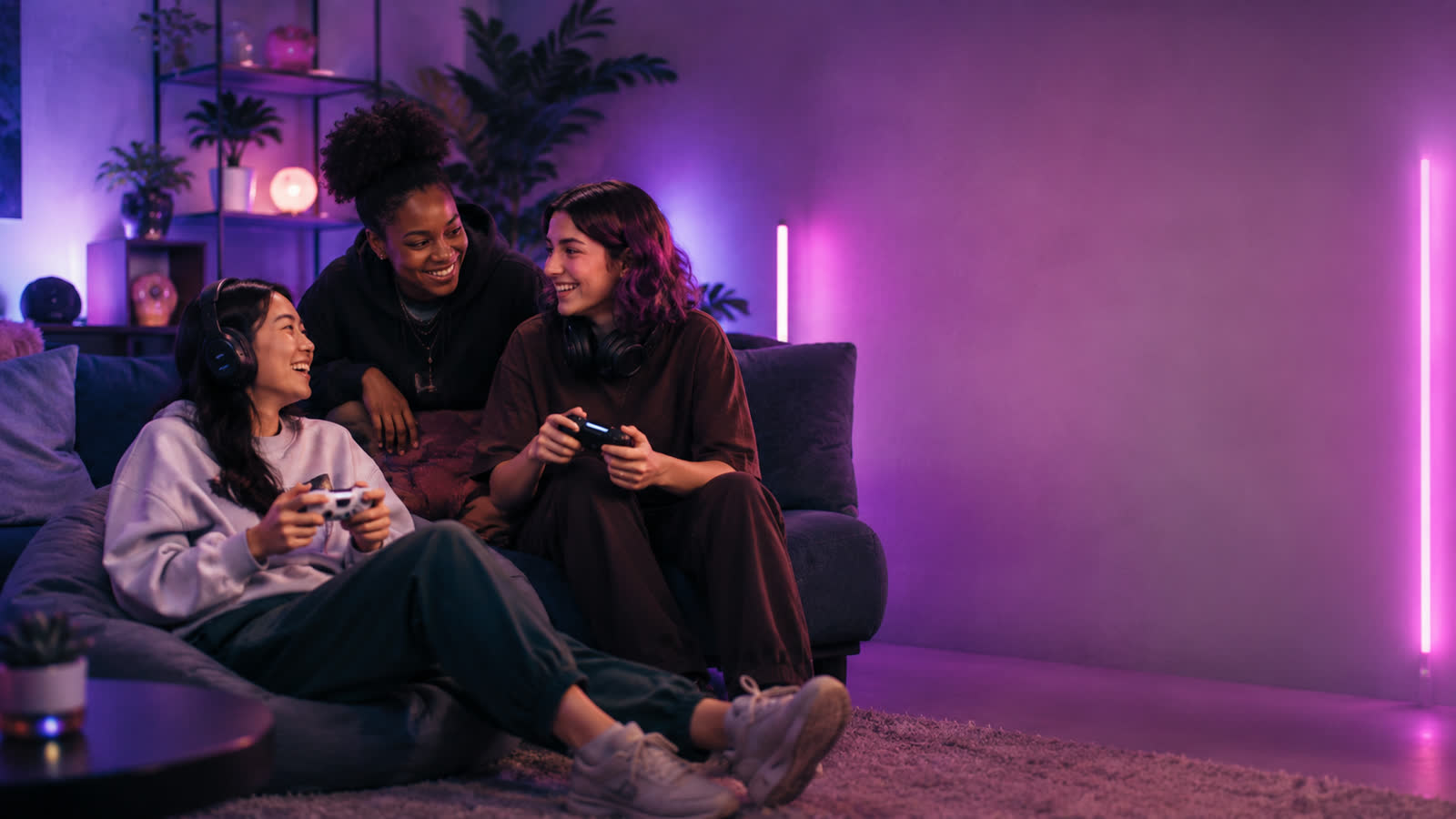 Drei Gamerinnen spielen lachend mit Controllern auf dem Sofa